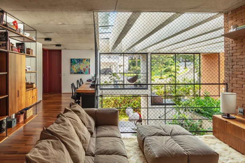 Living room with chain-link safety screen on mezzanine opening, exposed brick wall and timber built-in shelving