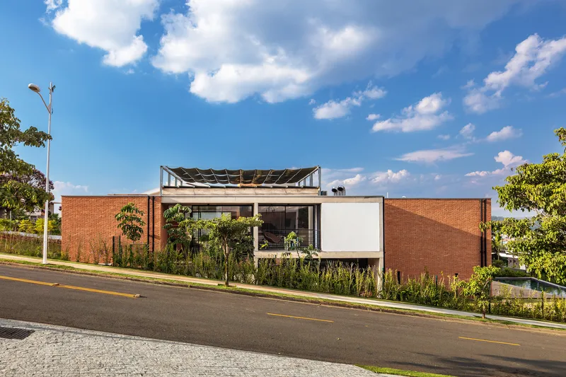 Facade composition with brick volumes, white panel, planted verge and exposed roof structure under blue sky