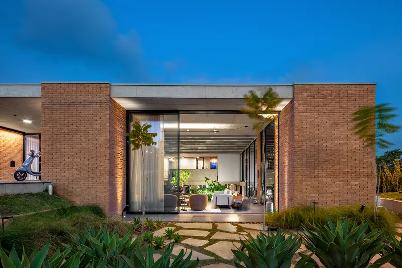 Entry portal framed by brick walls at dusk with planted stepping stones and exposed ceiling joists illuminated within