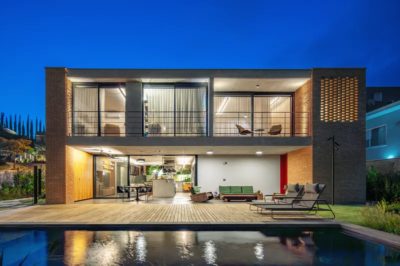 Rear facade with two-story glass walls and timber deck beside the swimming pool at dusk