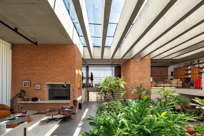 Double-height living space with central planted bed beneath exposed concrete beams and skylight