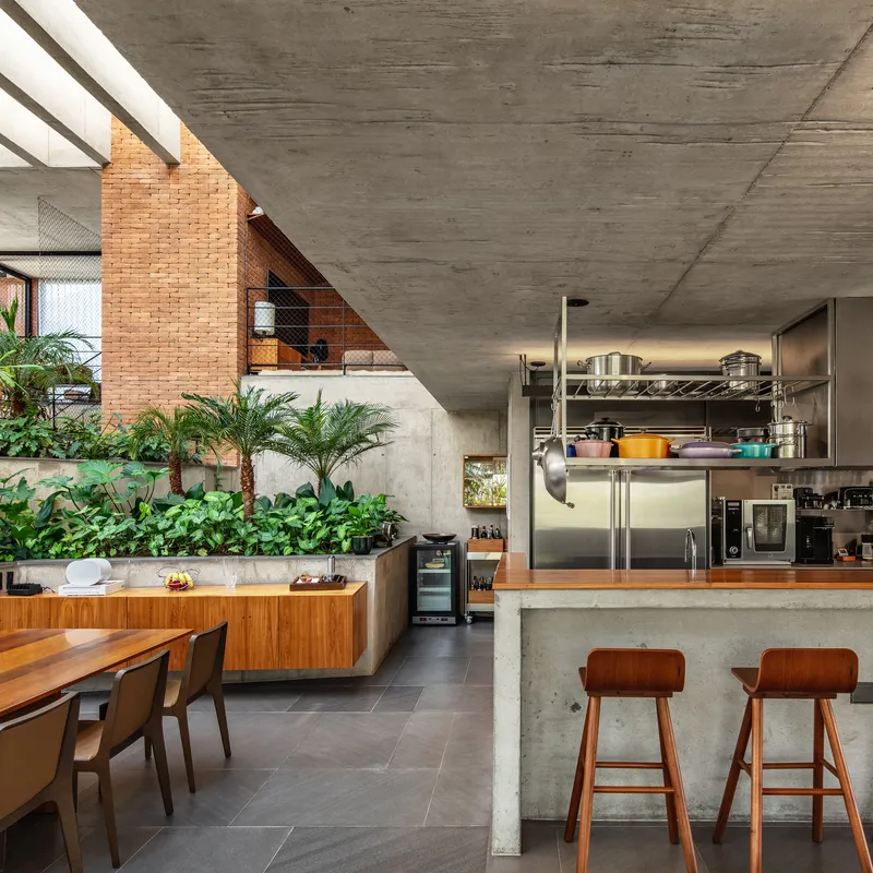 Open kitchen with stainless steel shelving and concrete island beneath angular ceiling beside planted wall