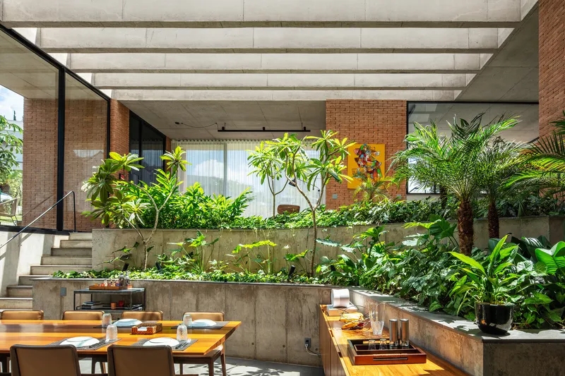 Dining area with timber table facing tiered concrete planters filled with foliage beneath skylight