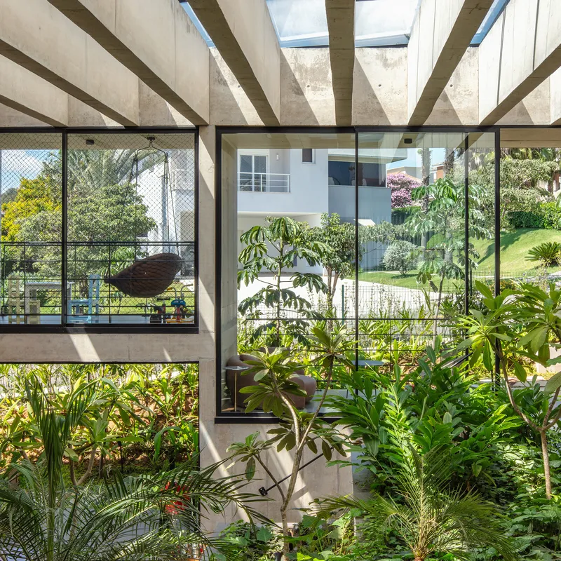 Covered planted courtyard with concrete beams overhead and floor-to-ceiling glazing framing garden views