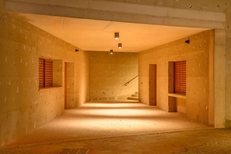 Interior corridor with rammed earth walls, wood shutters and warm light spilling across the floor at dusk