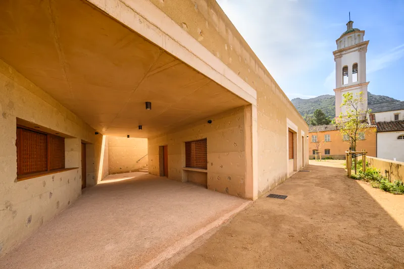 Covered entry passage with exposed concrete soffit and church bell tower visible beyond