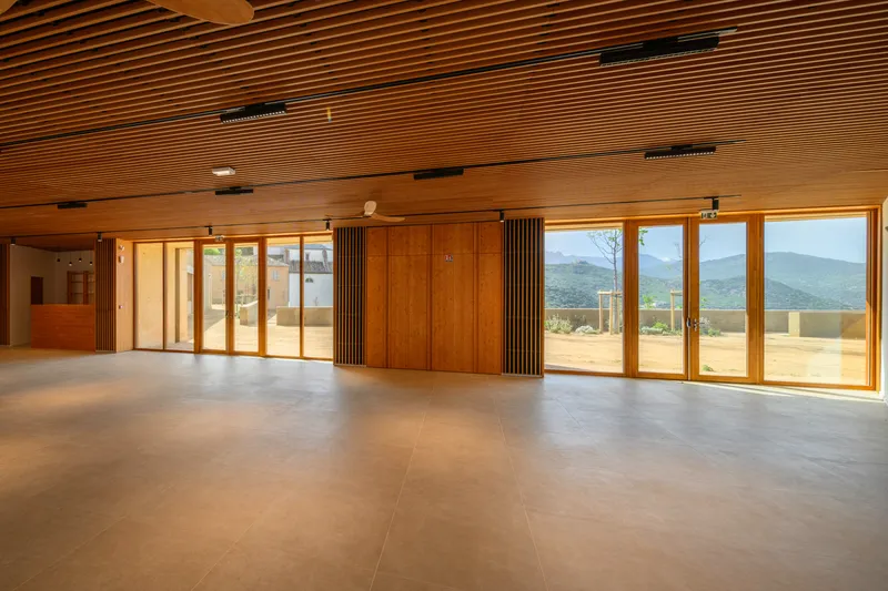 Interior hall with slatted timber ceiling and floor-to-ceiling windows framing distant mountain views