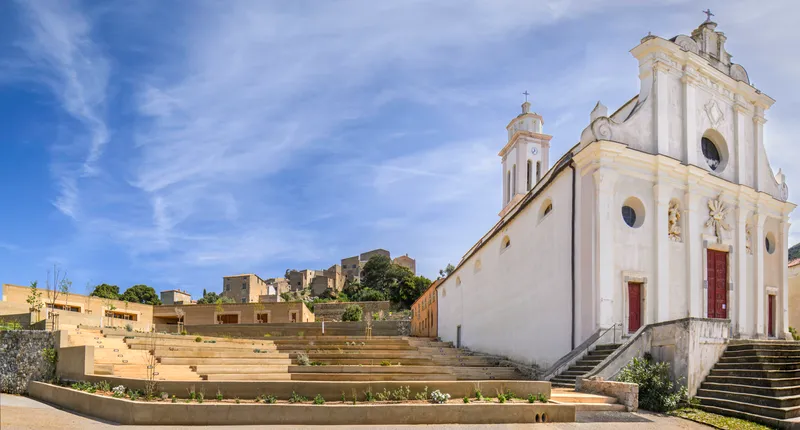 Wide concrete stepped terraces rising from the white church facade toward the village on the slope beyond