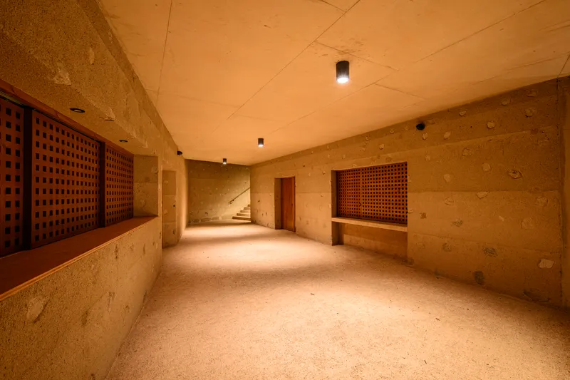 Basement corridor with rammed earth walls and timber lattice screens leading to a staircase