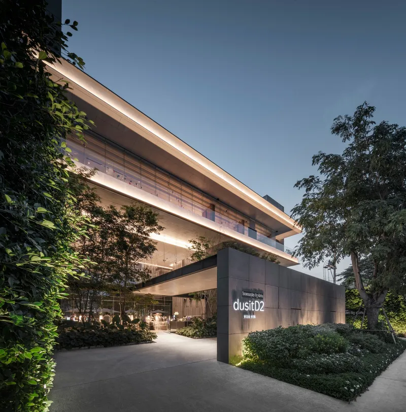 Entry approach with illuminated cantilevered floors framed by mature trees at dusk