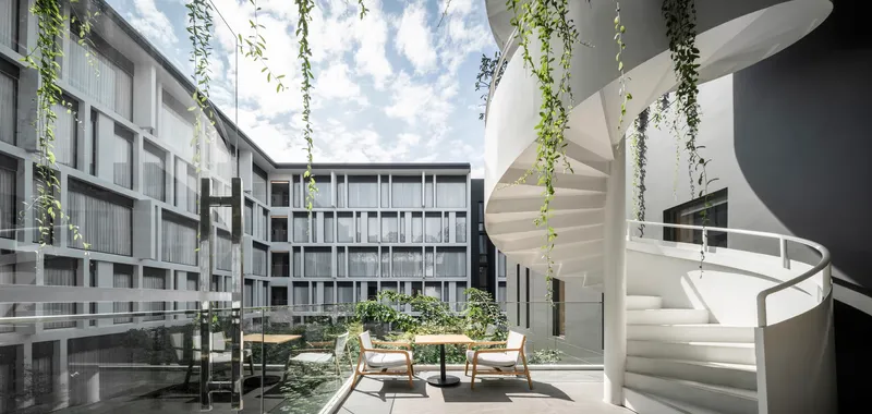 Interior courtyard with white spiral stair and cascading vines under open sky