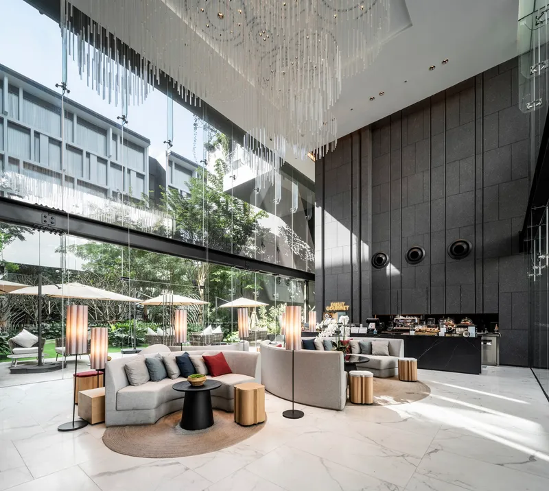 Double-height lobby with dark paneled wall and cascading crystal chandelier beside planted courtyard
