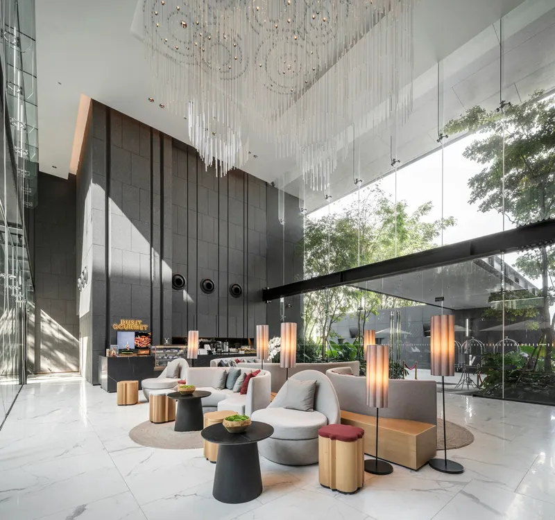Double-height lobby with cascading crystal chandelier, dark paneled walls, and floor-to-ceiling glazing opening to a landscaped courtyard