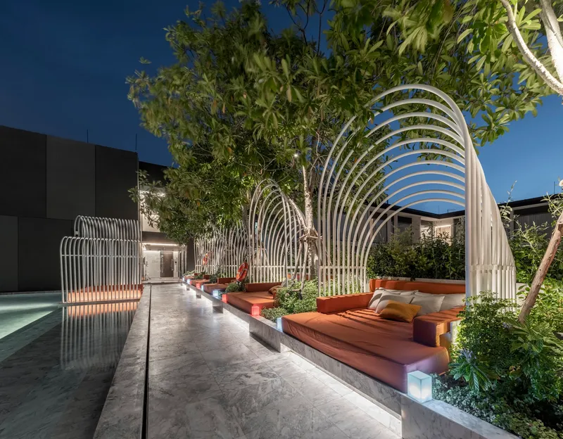 Outdoor terrace with white metal canopy structures, built-in cushioned seating, and reflecting pool at twilight
