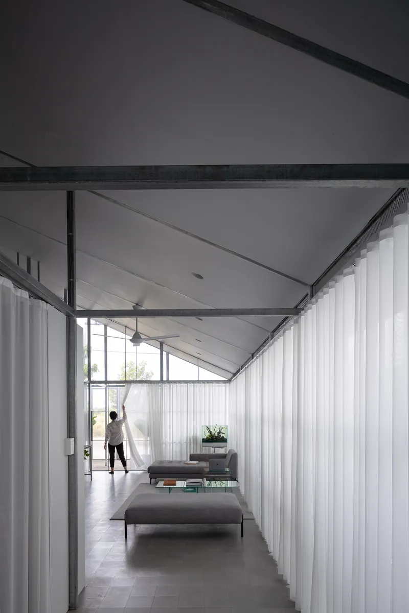 Interior corridor with exposed steel frame and white curtains flanking a figure at the window