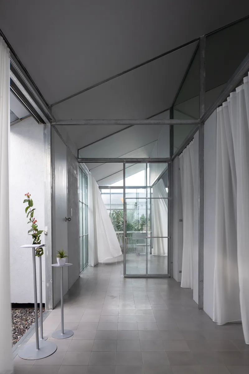 Narrow hallway with glass partitions, white curtains, and potted orchids on metal stands