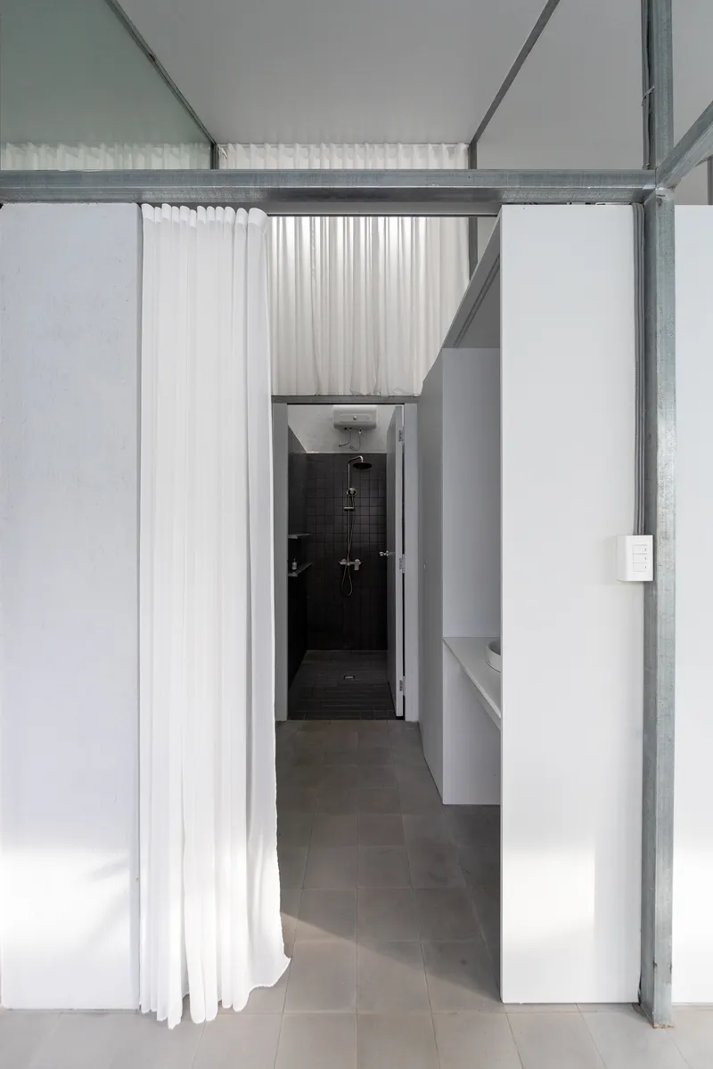 Passage with white curtain partially drawn revealing dark tiled shower enclosure under skylight
