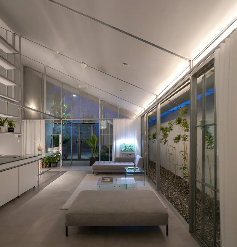 Living space with sloped ceiling and glazed walls flanking interior gravel courtyards at twilight