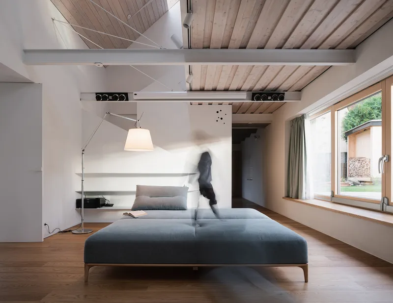 Living room with exposed timber ceiling beams and motion-blurred figure walking past daybed