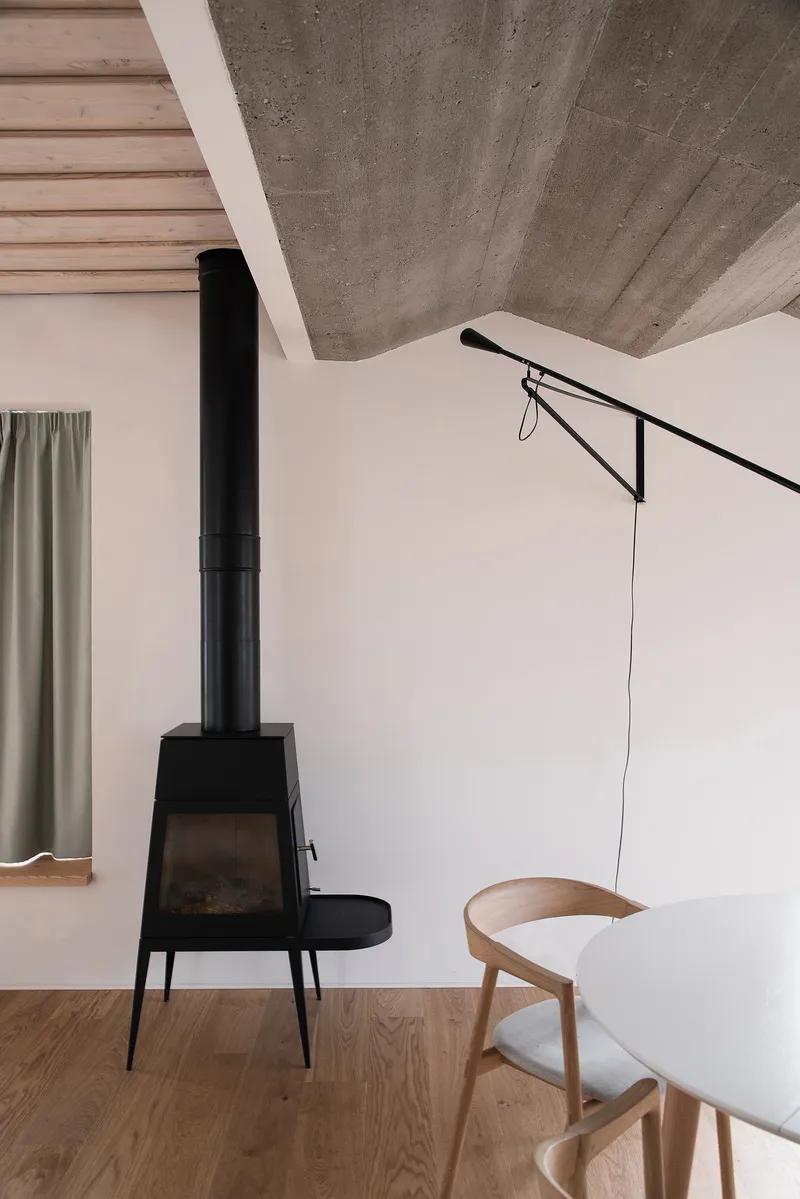Black freestanding wood stove beneath exposed concrete ceiling with timber slat panels and a wall-mounted lamp