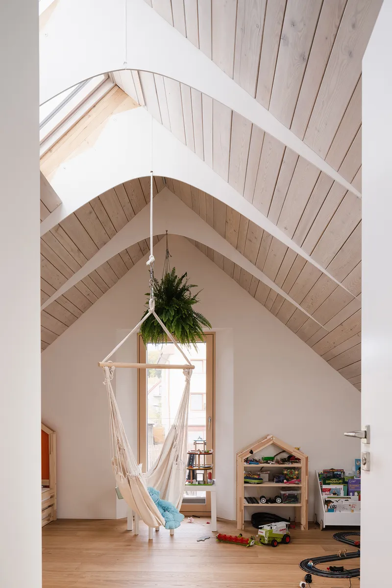 Gabled playroom with hanging macrame chair and timber ceiling framing a tall triangular window