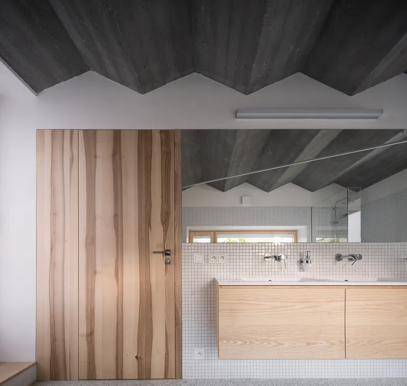 Bathroom with vertical timber door panels, white mosaic tile wall and exposed concrete sawtooth ceiling