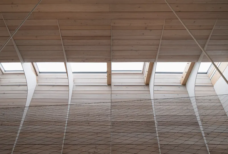 Interior view of the timber-clad sloped ceiling with rhythmic steel tension rods and skylights above