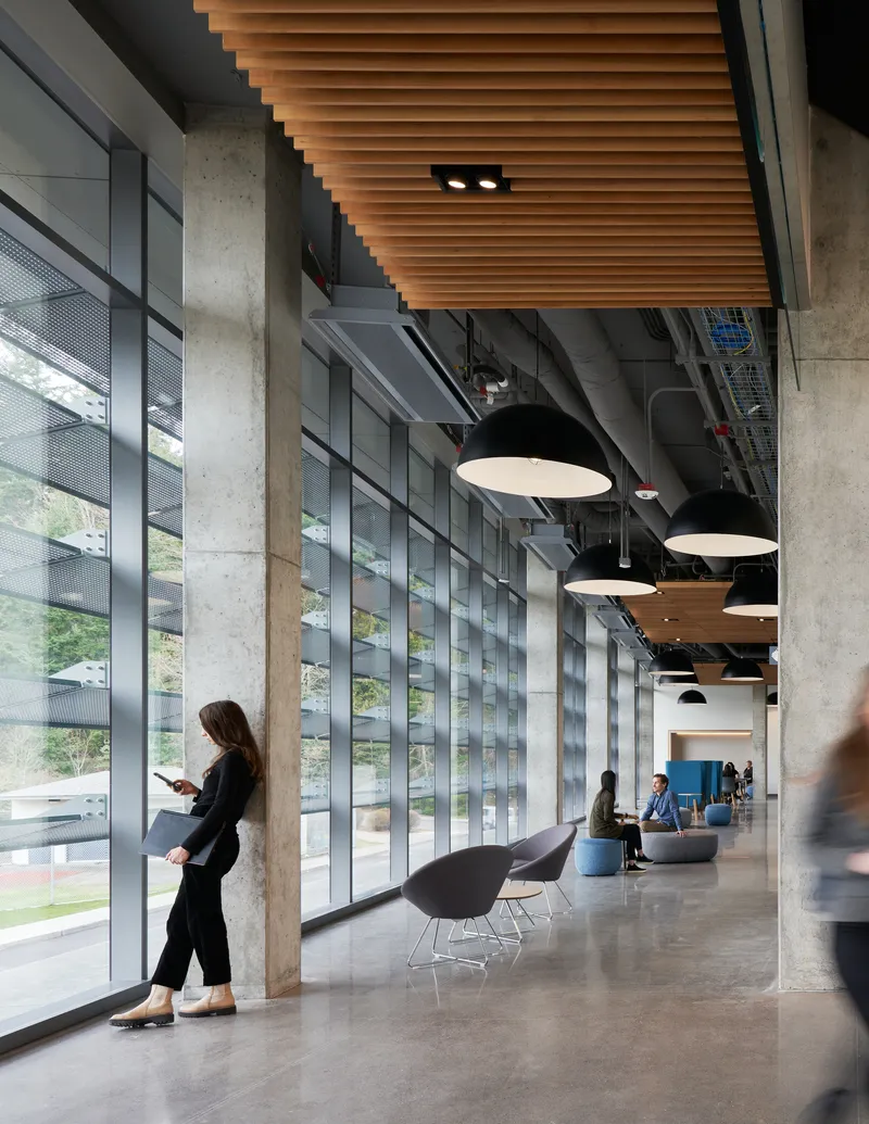 Interior corridor with concrete columns, timber slat ceiling and pendant lights alongside horizontal louver glazing