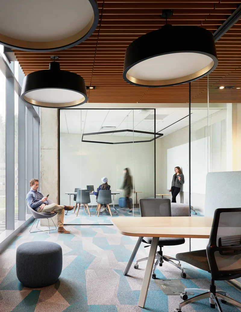 Open workspace with timber slat ceiling, pendant fixtures and hexagonal carpet pattern visible through glass partitions