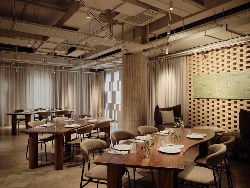 Dining room with timber tables, upholstered chairs and basketweave wall beneath an exposed structural ceiling