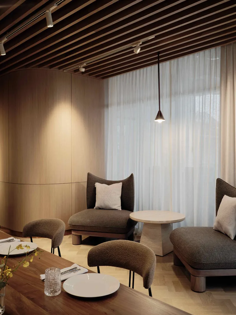 Lounge seating area with low chairs and slatted timber ceiling beneath a single pendant light