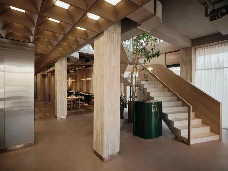 Interior lobby with timber vaulted ceiling, vertical wood-clad columns, and a stair with green planters