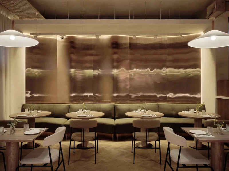 Banquette seating along translucent backlit wall panels with round tables and pendant lights overhead