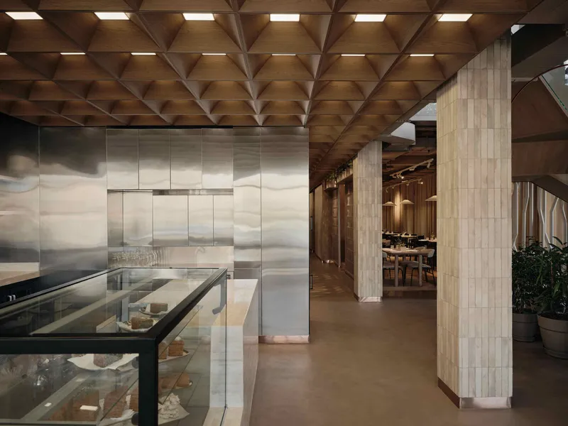 Geometric coffered wood ceiling above reflective metal wall panels and glass display case in corridor