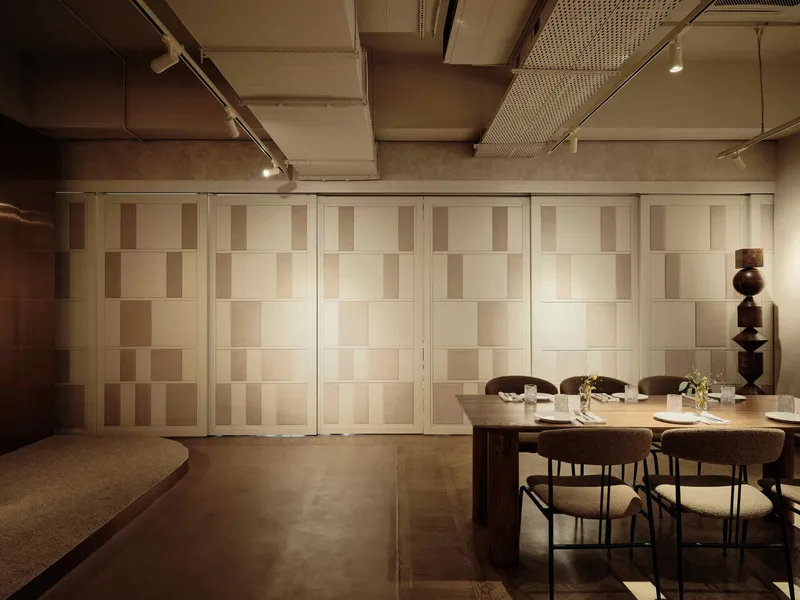 Folding panels with alternating wood tones beside a dining table and sculptural wooden floor lamp