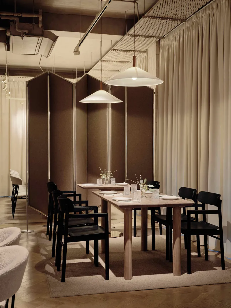 Dining table under white pendant lights with tall brown fabric wall panels behind