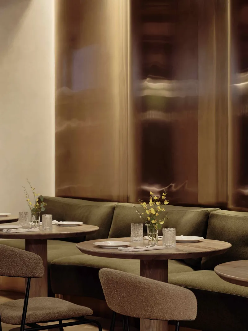 Curved banquettes and round tables with glazed brown wall partitions in soft lighting