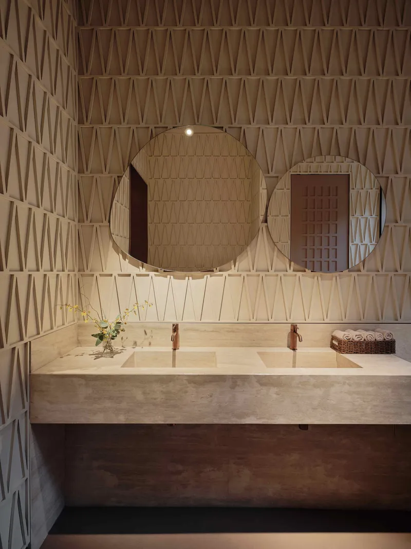 Bathroom vanity with stone counter and round mirrors against a triangular lattice wall