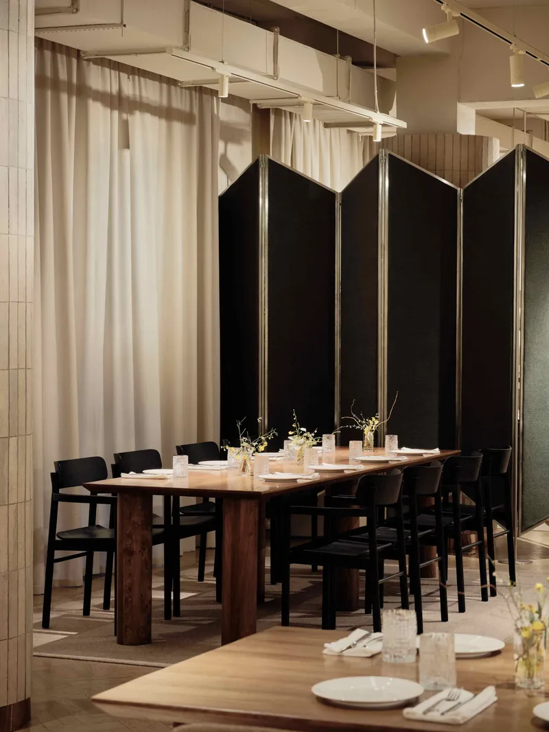 Dining area with timber table, black chairs, and tall black folding screens against sheer curtain backdrop