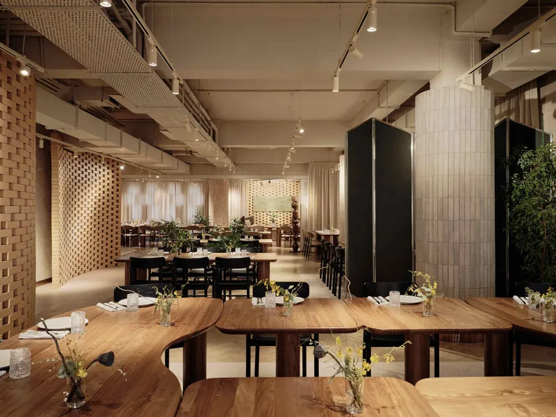 Wide view of dining hall with exposed ceiling ducts, timber screens, and rows of set tables