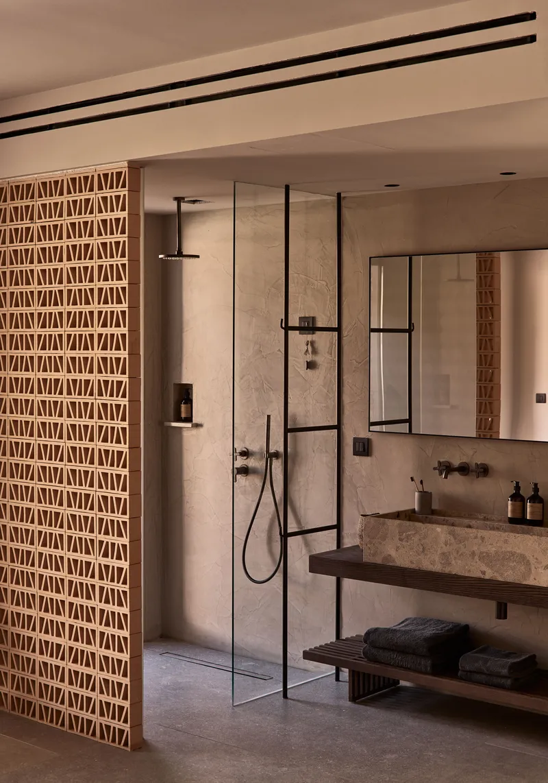 Bathroom with geometric lattice screen, frameless glass shower enclosure, and stone vanity beneath linear ceiling tracks