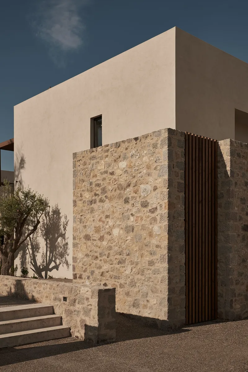 Corner facade combining pale stucco upper volume with rough stone lower wall and vertical timber screen