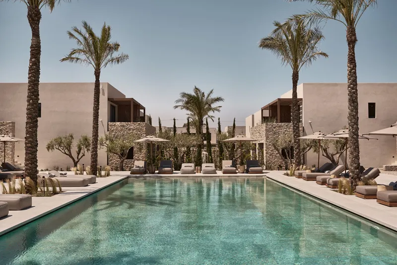 Central swimming pool flanked by symmetrical stone pergolas and lounge seating under palm trees