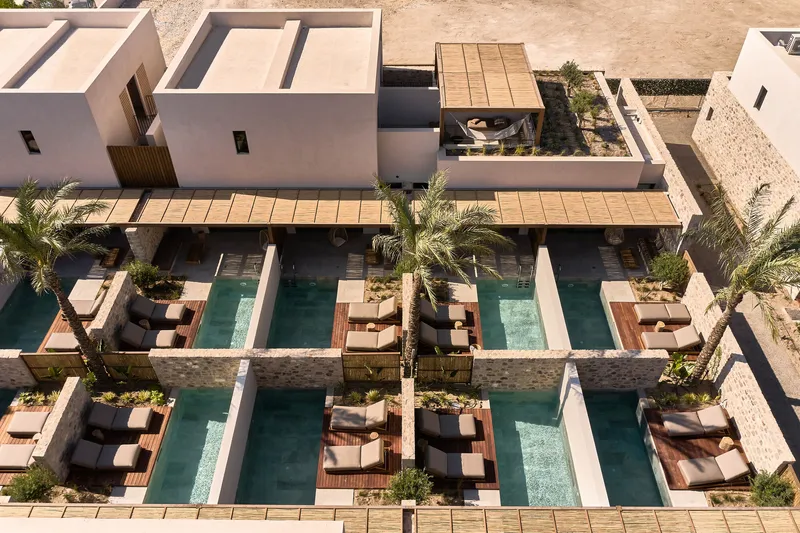 Aerial view of courtyard pools with timber decking and palm trees between white stucco volumes