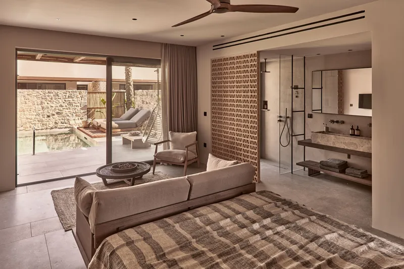 Guest suite with glass-enclosed bathroom opening onto a courtyard terrace with stone wall and palm tree