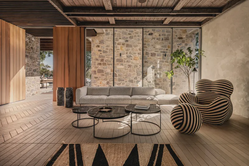 Living area with herringbone timber floor and full-height glazing overlooking stone courtyard wall in afternoon light
