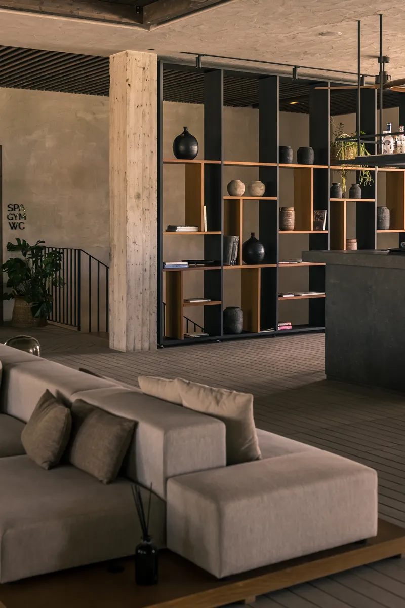Freestanding timber shelving unit displaying ceramics next to a textured concrete column with exposed beam ceiling