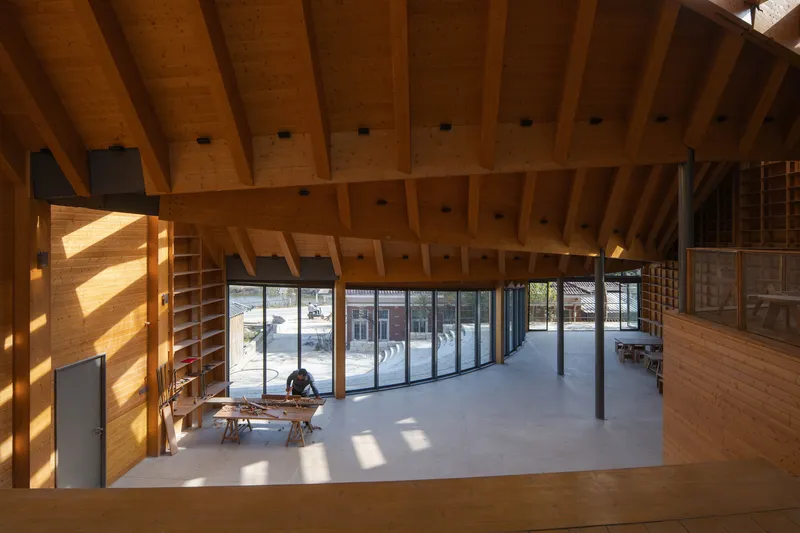 Double-height interior space with exposed timber beams and curved glazing facing a courtyard