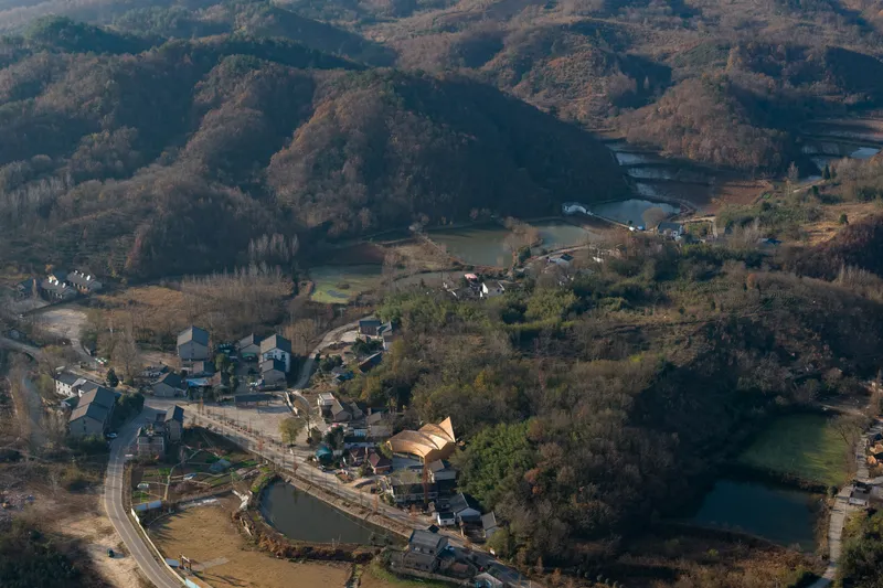 Aerial view of the curved roof structure nestled in a village by a lake
