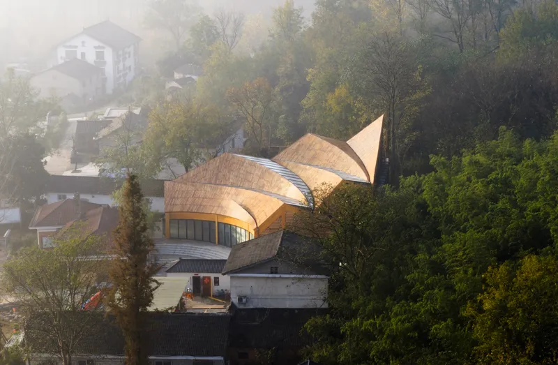 Elevated view of the three-lobed timber roof emerging from the hillside village in morning fog